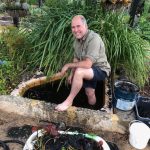 Photo of a male gardener with one foot in the frog pond and the other outside.