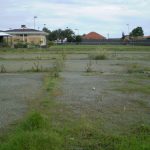 Photo of the site with gravel and weeds.